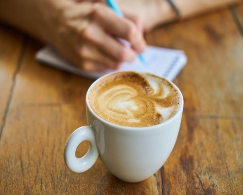 A person writing notes peacefully at a wooden desk with a morning coffee in a Mexican cafe